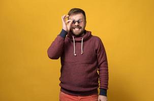 Cheerful Caucasian bearded man holds toy sunglasses like pince-nez to his eyes, with a bizarre grimace and grin. Yellow background. photo