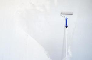 Sponge roller on a wooden stick repaints the wall gray. Home renovation. Copy space. photo
