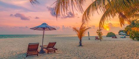 Tranquil romantic beach scene. Couple chairs umbrella, exotic tropical beach landscape for background wallpaper. Panoramic summer vacation holiday banner. Resort shore, palm leaves sunset sea sky sand photo