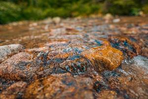 Abstract closeup streaming bubbles over riverbed with colorful stones. Closeup nature background motion, speed, varying textures and vibrant colors. Drops streams of water scatter over the stone. photo