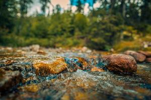 Abstract closeup streaming bubbles over riverbed with colorful stones. Closeup nature background motion, speed, varying textures and vibrant colors. Drops streams of water scatter over the stone. photo