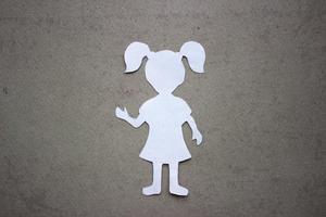 The form of a girl in a dress and with ponytails made of white paper, cut by hand. In the center of the photo