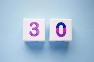 Close-up photo of a white plastic cubes with a colorful number 30 on a blue background. Object in the center of the photo