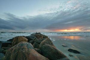 Sunset on the beach in Denmark. Stone groyne in the foreground. Walk on the coast photo