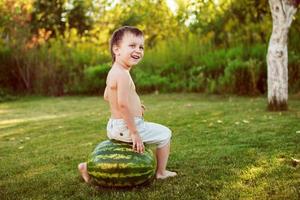 portrait of happy child boy with a large whole watermelon in the back yard photo