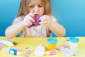 Blonde girl hold purple slime isolated on blue background. child playing with slime toy. Making slime. Copy space. photo