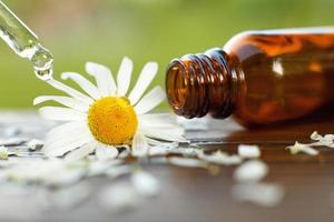 Chamomile essential oil brown glass bottle with a pipette with drop on a wooden table outdoor. photo