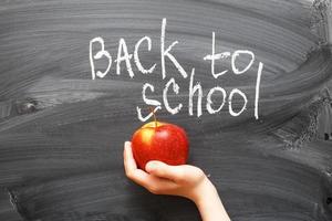 mano de niño sosteniendo una manzana cerca de la pizarra. fondo de concepto de regreso a la escuela foto