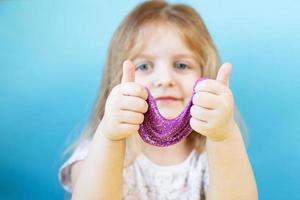 Blonde girl hold purple slime isolated on a blue background. child playing with a slime toy. Making slime. Copy space. photo