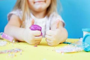 Blonde girl hold purple slime isolated on a blue background. child playing with a slime toy. Making slime. Copy space. photo