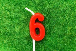 candle in the form of number 6 on the green grass background, a place for a greeting text photo