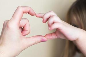 forma de corazón creada a partir de las manos de la niña y las manos de su madre sobre fondo beige. foto