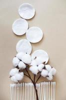 almohadillas de algodón de flores de algodón esponjoso y bastoncillos de algodón sobre fondo beige con espacio de copia. producto higiénico desechable foto