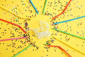 birthday party.baby stroller with stars confetti sequins and multicolored drinking straws on yellow background photo