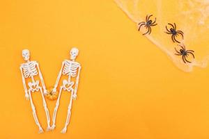 esqueletos con calabaza, telaraña y arañas negras sobre fondo naranja. concepto de halloween foto