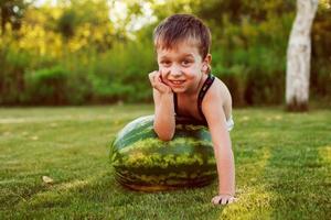 portrait of happy child boy with a large whole watermelon in the back yard photo