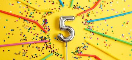 fiesta de cumpleaños de cinco años. número cinco con forma de estrellas y pajitas sobre fondo amarillo foto