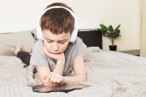 child boy lying on bed with pc tablet with wireless headphones photo