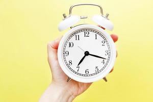 female holding white alarm clock in her hand on yellow background photo