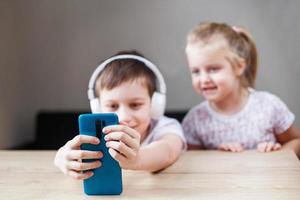 two happy children playing on the smartphone in headphones. people, children and technology concept photo