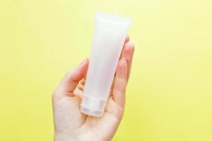 Female hand holding cream tube cosmetic products on yellow background photo