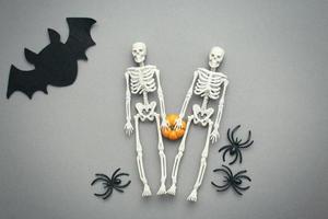 esqueletos con calabaza, murciélago y arañas negras sobre un fondo gris. concepto de halloween foto