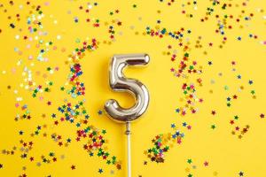 fiesta de cumpleaños de cinco años. número cinco con confeti multicolor en forma de estrellas sobre un fondo amarillo foto