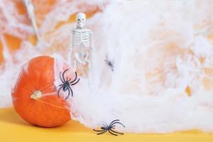 Halloween pumpkin with spider web, skeleton and black spiders on orange background. photo