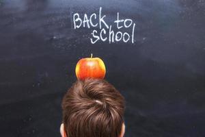 una manzana en la cabeza de un niño cerca de la pizarra. fondo de concepto de regreso a la escuela foto