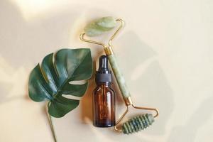 Massage quartz roller for the face of natural nephritis with serum oil with monstera leaves on beige background. photo