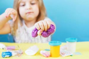 Blonde girl hold purple slime isolated on blue background. child playing with slime toy. Making slime. Copy space. photo