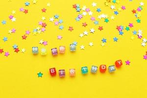 inscription happy birthday and multicolored confetti in the form of stars on yellow background photo