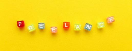 word freelance made from multicolored plastic cubes of beads on yellow background. banner photo