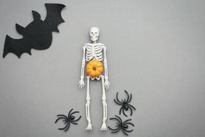 esqueleto con calabaza, murciélago y arañas negras sobre un fondo gris. concepto de halloween foto