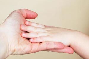 Close up of mothers hand holding babies hand Isolated on beige background. photo