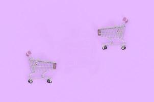 Shopping addiction, shopping lover or shopaholic concept. Small empty shopping cart lies on a pastel colored paper background. Flat lay minimal composition, top view photo