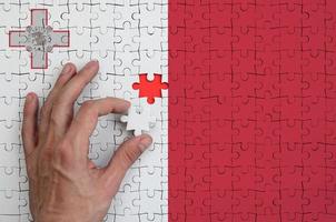 Malta flag is depicted on a puzzle, which the man's hand completes to fold photo