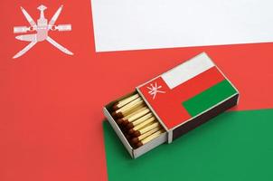 Oman flag is shown in an open matchbox, which is filled with matches and lies on a large flag photo