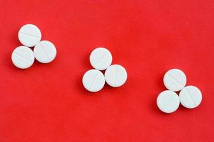 Several white tablets lie on a bright red background in the form of three triangular arrows. Background image on medicine and pharmaceutical topics photo