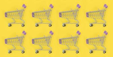 Shopping addiction, shopping lover or shopaholic concept. Many small empty shopping carts perform a pattern on a pastel colored paper background. Flat lay composition, top view photo