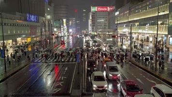 shinjuku, tokio, japón 2019-11-22. la gente cruza la calle mientras llueve y hay autos en la carretera. en la ciudad de shinjuku, tokio, japón. video