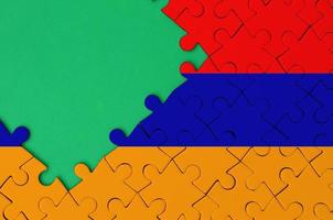 Armenia flag is depicted on a completed jigsaw puzzle with free green copy space on the left side photo