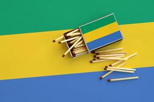 Gabon flag is shown on an open matchbox, from which several matches fall and lies on a large flag photo
