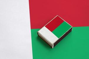 Madagascar flag is pictured on a matchbox that lies on a large flag photo