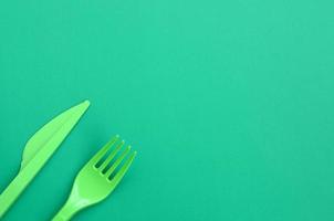 Disposable plastic cutlery green. Plastic fork and knife lie on a green background surface photo