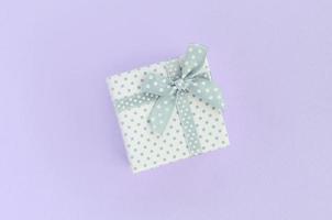 Small white gift box with ribbon lies on a violet background. Minimalism flat lay top view photo