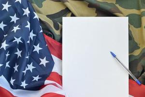 Blank paper lies on United States of America flag and folded military uniform jacket. Military symbols conceptual background banner and copy space photo