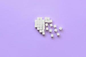 A broken heart made of sugar cubes lies on a trendy pastel violet background photo