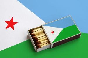 Djibouti flag is shown in an open matchbox, which is filled with matches and lies on a large flag photo