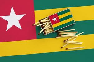 Togo flag is shown on an open matchbox, from which several matches fall and lies on a large flag photo